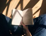 Mani che sfogliano un libro aperto, illuminato da raggi di sole. Un momento di pace e consigli libri.