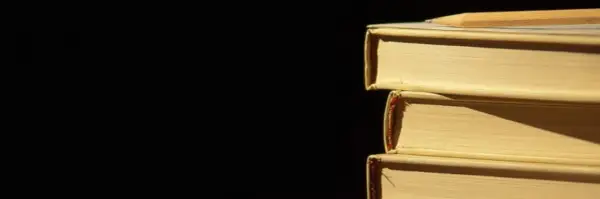 Libri impilati, un libro in cima con una matita. La luce crea ombre, un po' come l'anastrofe figura retorica che inverte l'ordine per enfasi.