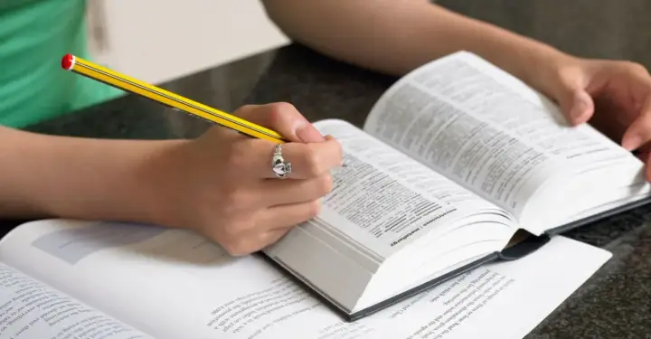 Mani che studiano un dizionario, scrivendo con una matita. Scoprire parole italiane affascinanti è un viaggio.