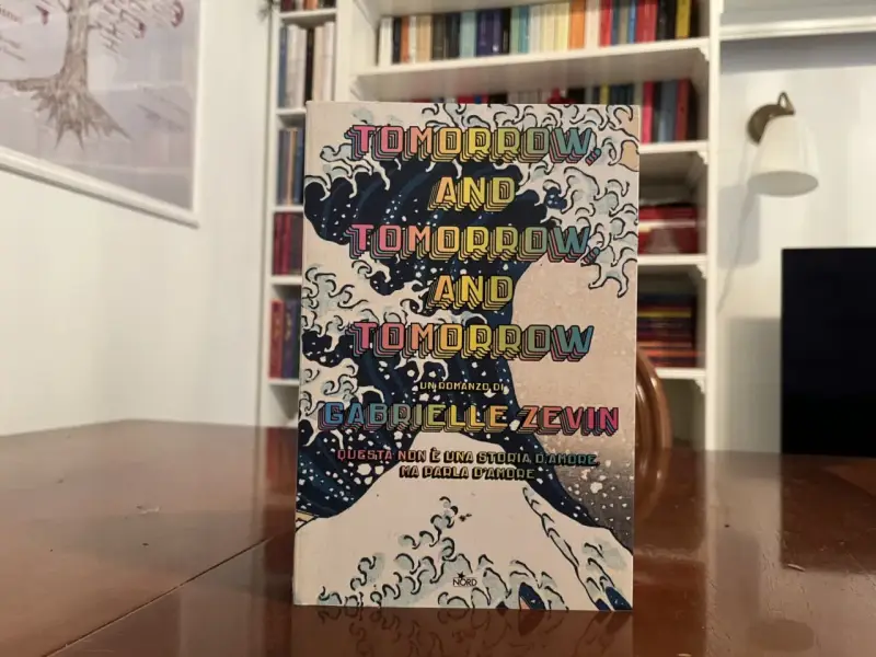 Copertina del libro "Tomorrow, and tomorrow, and tomorrow" di Gabrielle Zevin, con onde stilizzate e testo ripetuto.